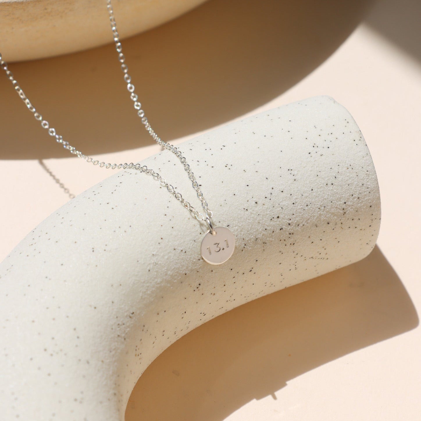 sterling silver hand stamped round disc charm on a delicate chain necklace on a light surface