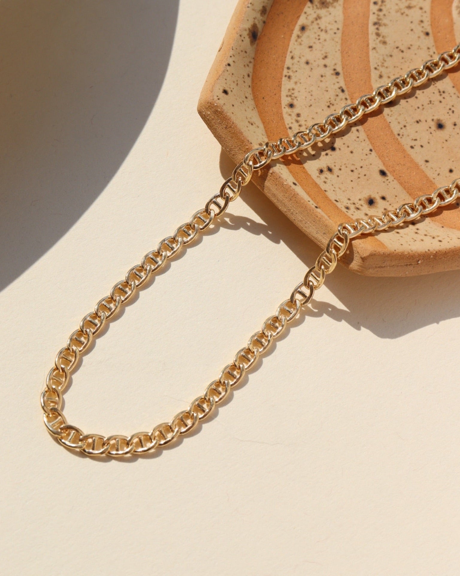 The Marina Chain by Token Jewelry, a modern classic with interlocking oval-shaped links, photographed laying over a patterned ceramic dish