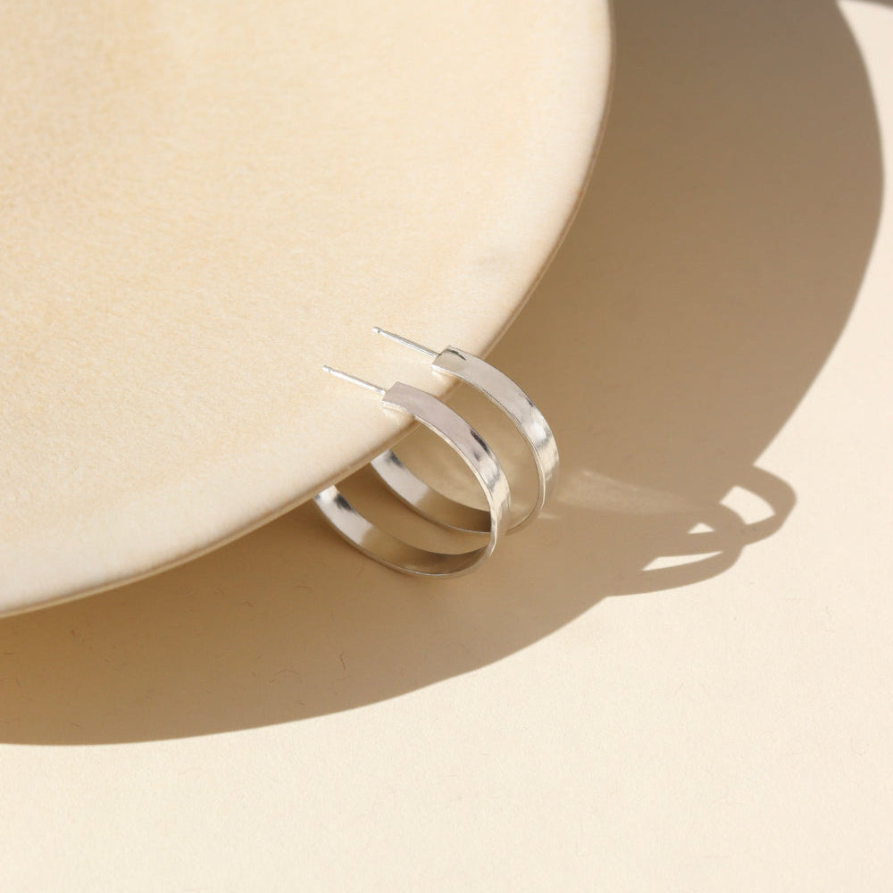 A medium thick hammered sterling silver hoop displayed on a cream display. 