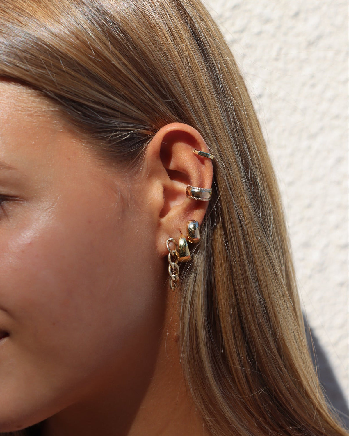 Women wearing a gold fill earring stack with chain studs, hoops, and huggies with a textured ear cuff and cartilage hoop