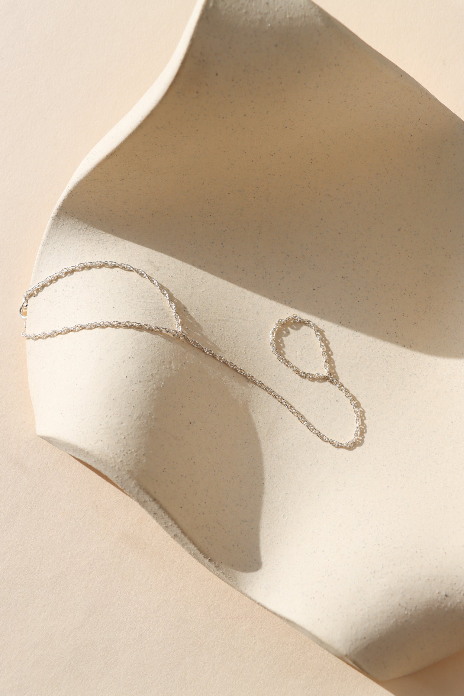 sterling silver hand chain laid on a wavy dish in the sunlight