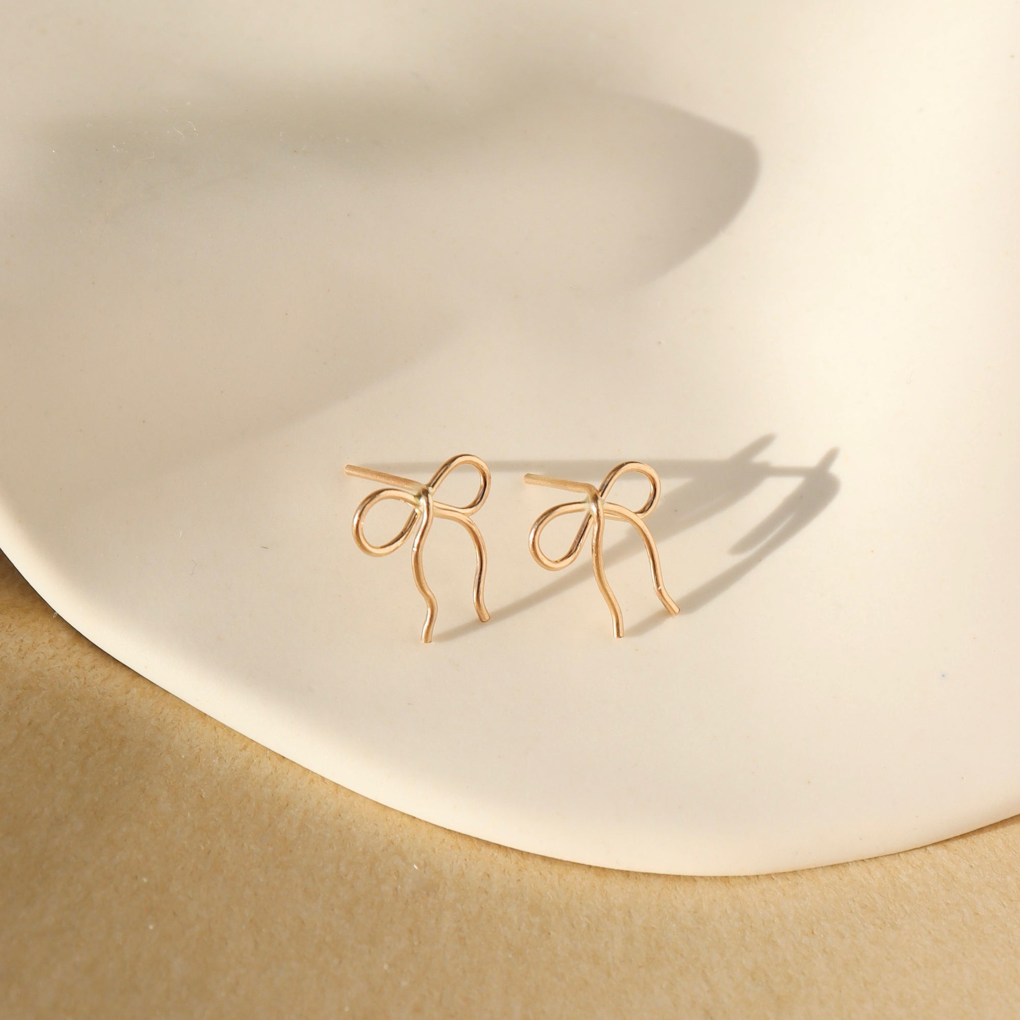 14k gold fill hand shaped bow stud earrings on a light dish