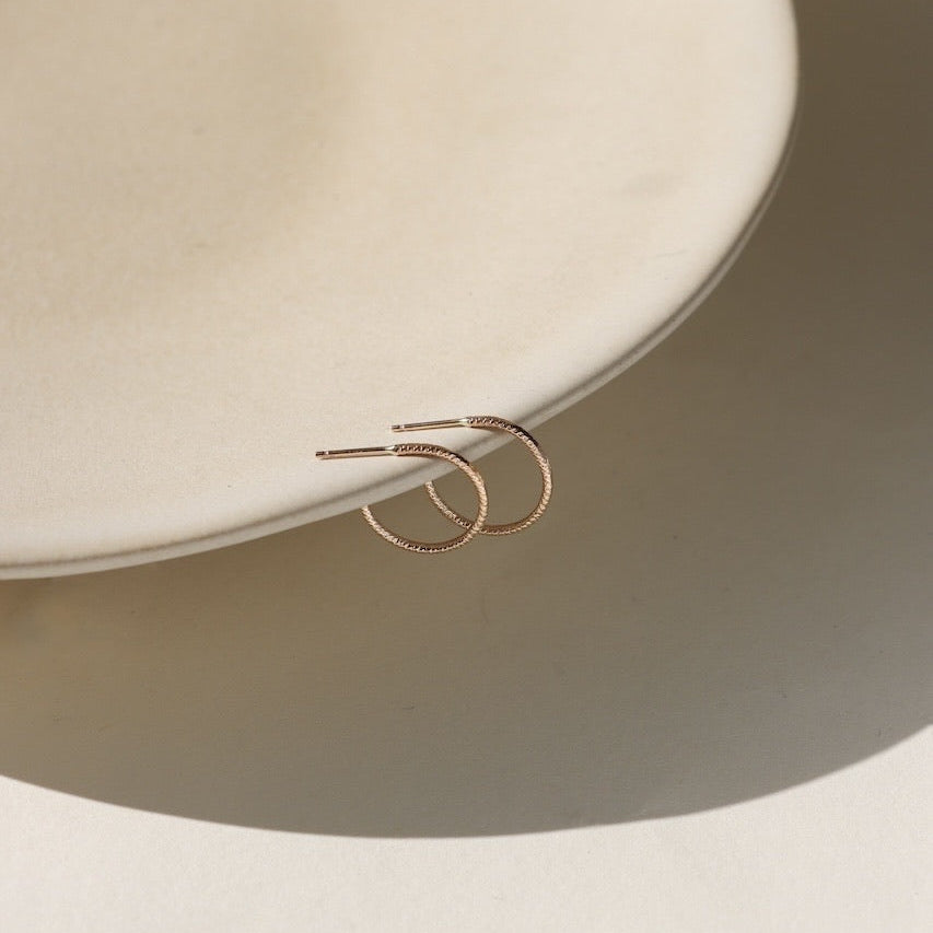 Gold hoop earrings on a light beige plate with a neutral background