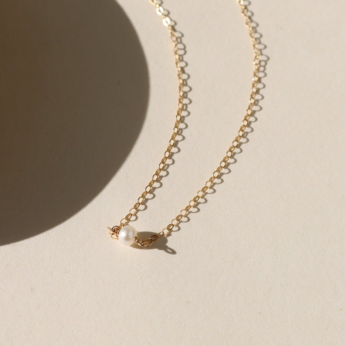 Gold chain necklace with a single pearl pendant on a beige background