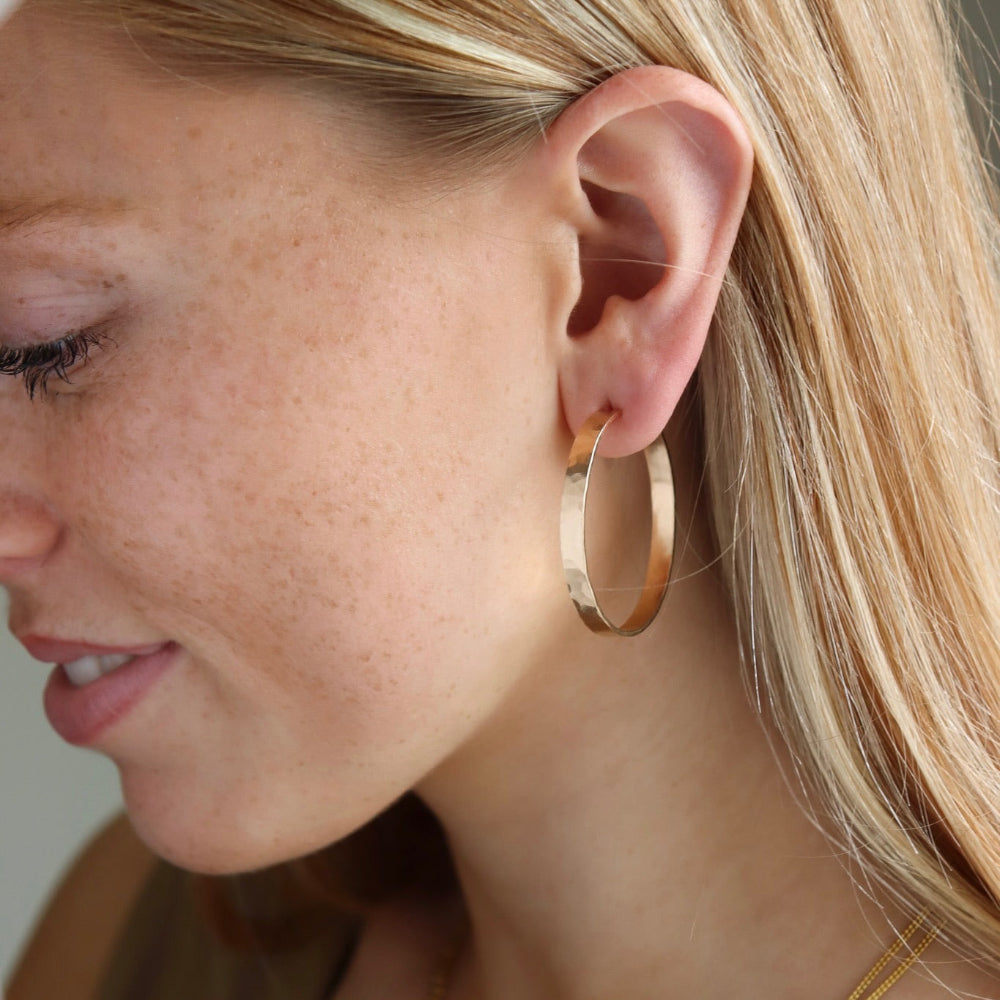 Model wearing the large pair of mirage hoops, featuring a thick hammered wire. 