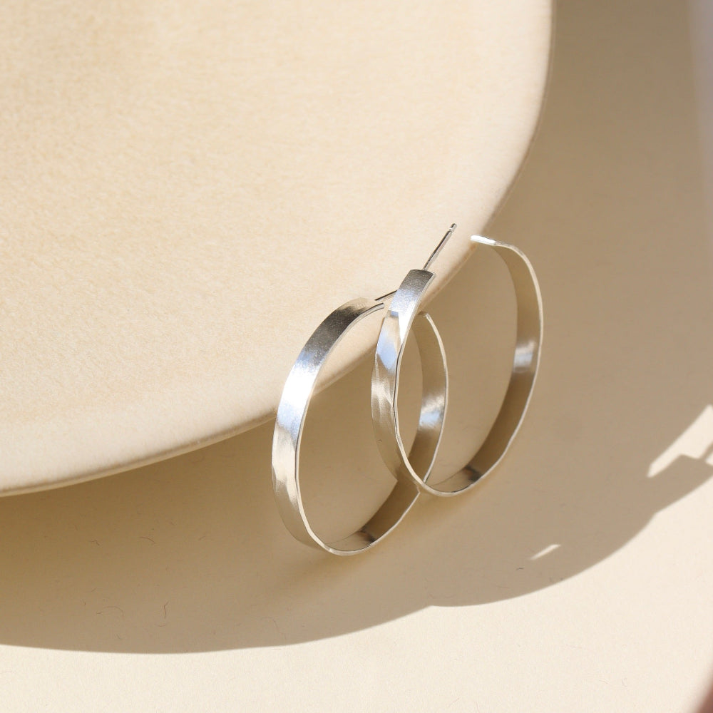 A large thick hammered sterling silver hoop displayed on a cream display. 