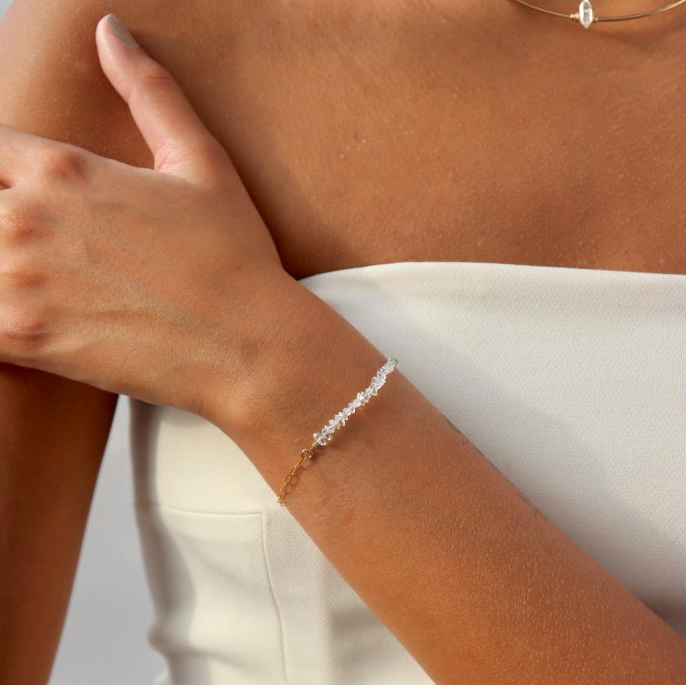 A gold bracelet with a strand of Herkimer stones with a delicate gold linked chain. Bracelet is taken on a model with a white tube top, also featuring our Collarbone Herkimer Necklace. 