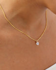 Model wearing the lumi necklace. Necklace features a gold curb chain with a moonstone hanging in the center. Model is wearing a white tube top. 