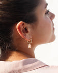 Pink pearl earrings are taken on a brunette model wearing a light pink blouse. 