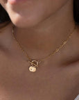 model wearing 14k gold fill monogram toggle necklace. This necklace features the narrow link chain connected by a toggle with the monogram disc.