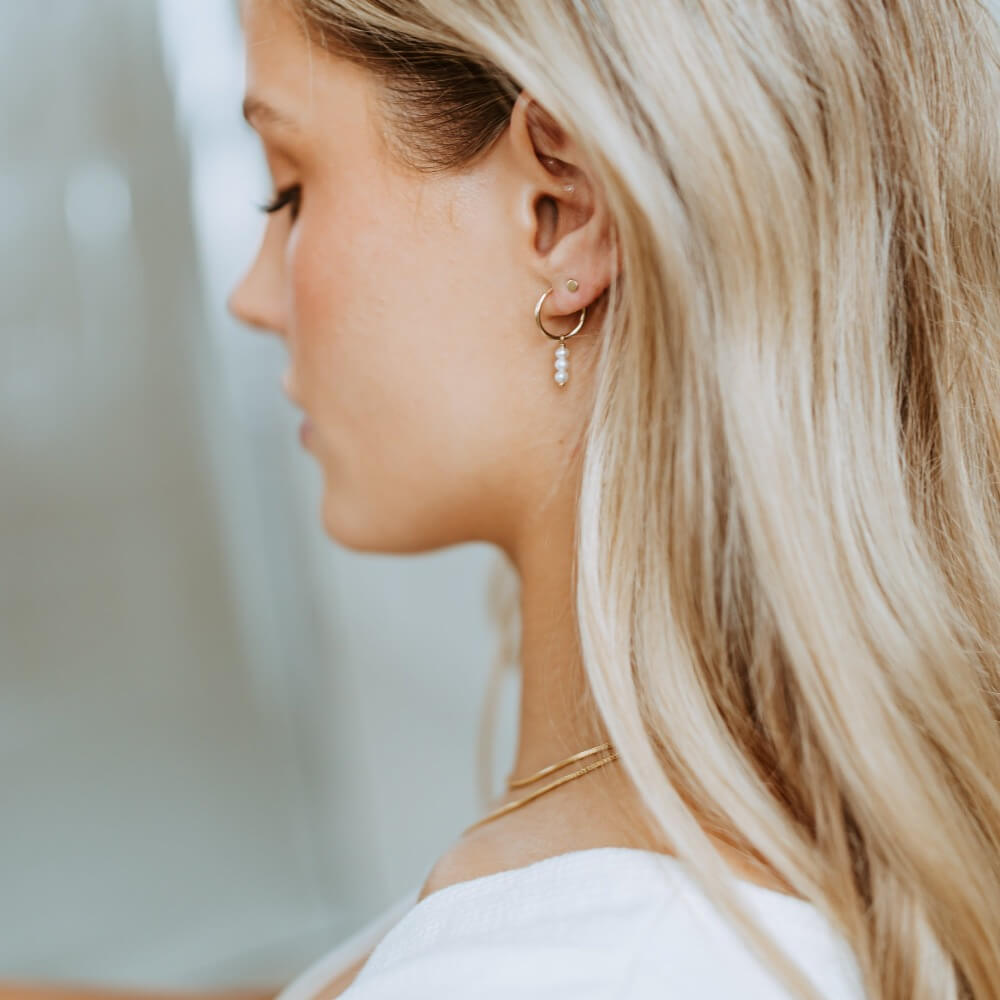 Model wearing 14k gold fill Petite Pearl Hoops, these earrings feature a petite hoops with three mini pearls hanging from the hoop. 