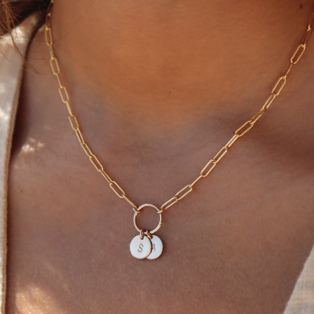 A textured chain-link style 14k gold fill necklace chain featuring a gold hoop, from which hangs two stamped discs. photographed on a model