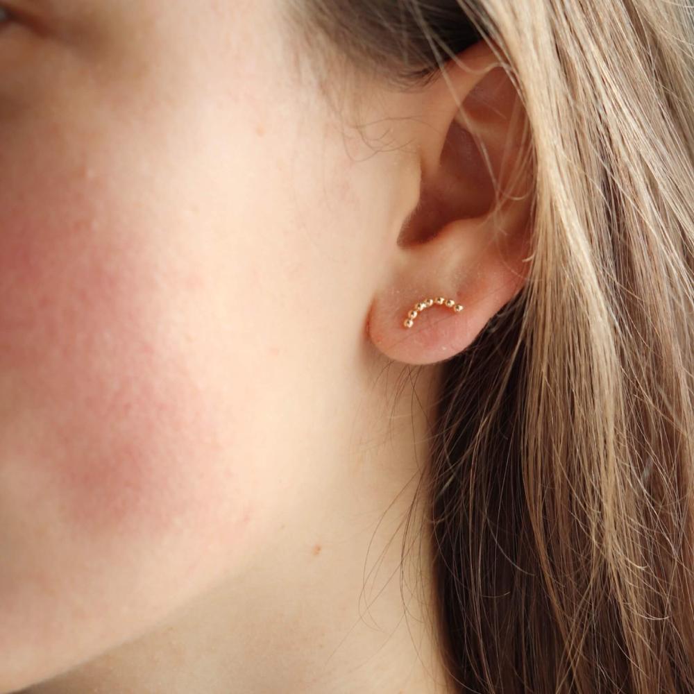 Model wearing 14k gold fill sequin arcs. Handmade by Token Jewelry in Eau Claire, Wisconsin. This earring features a stud like earring with an arc type shape. This arc features the sequin wire featured in multiple other pieces.- token jewelry