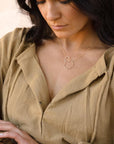 Brunette model wearing the unity necklace. This necklace features a dainty gold chain with a large and small circle connecting in the center. 