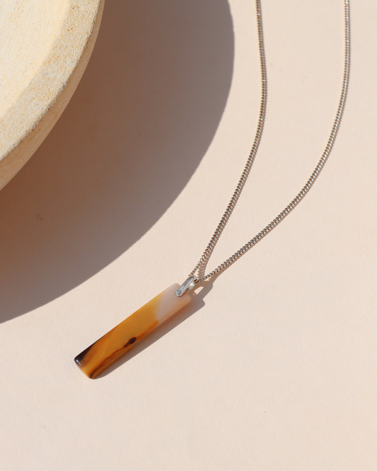 Rectangular amber and cream stone pendant necklace on a silver chain, photographed in warm sunlight.
