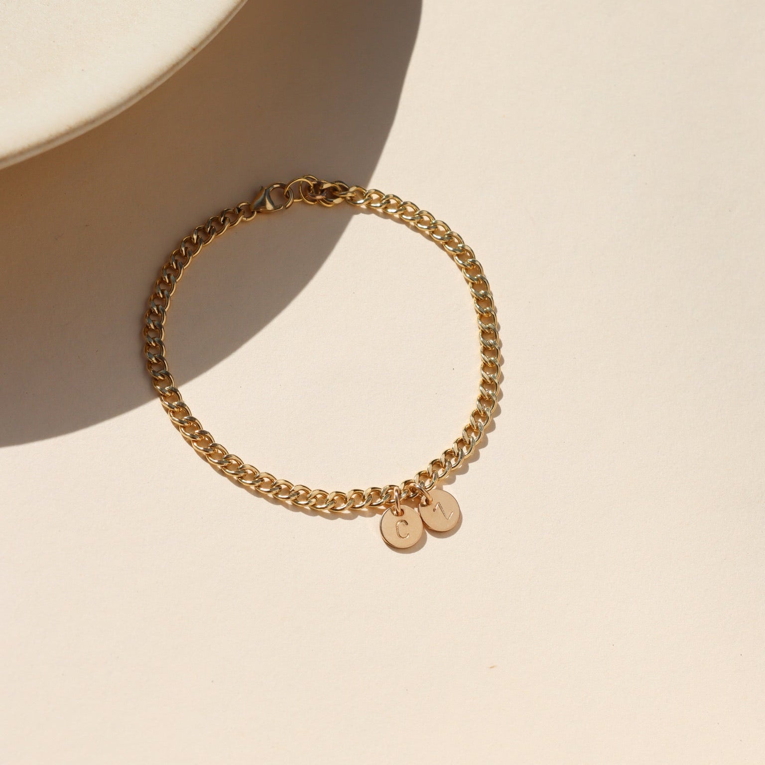 14k gold fill curb chain bracelet with hand stamped round disc charms on a light table