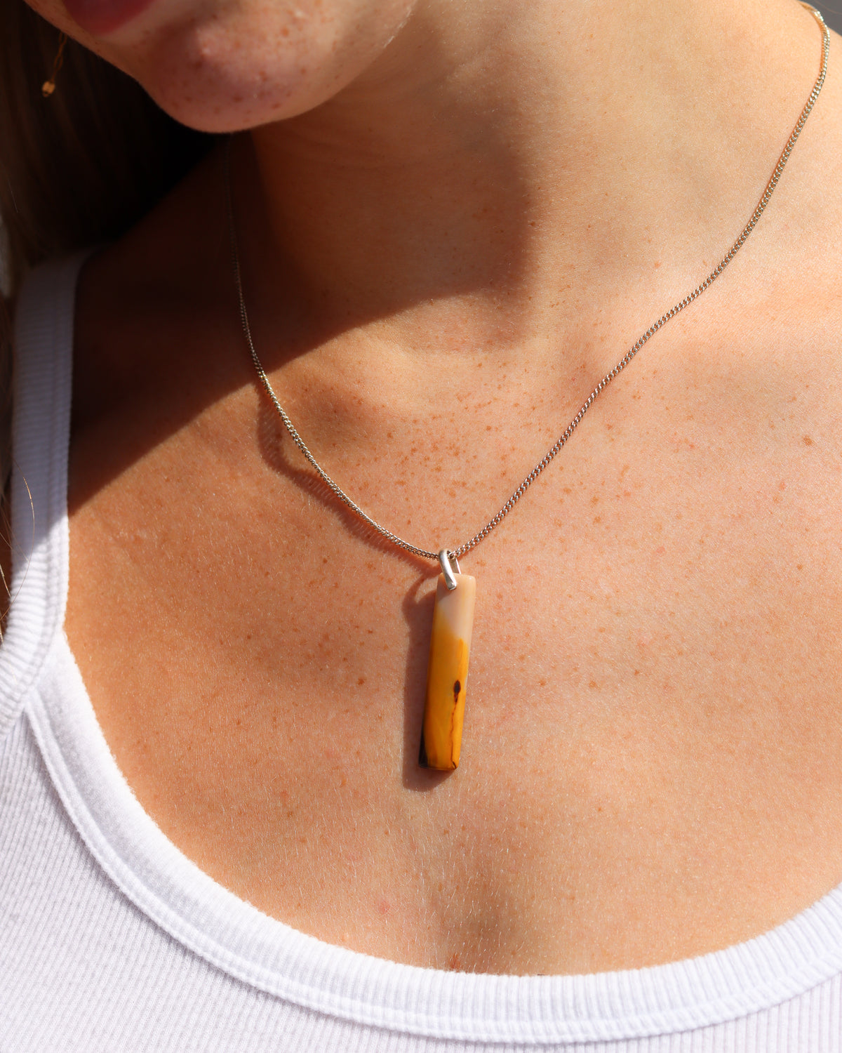 Rectangular amber and cream stone pendant necklace on a silver chain, worn in warm sunlight.