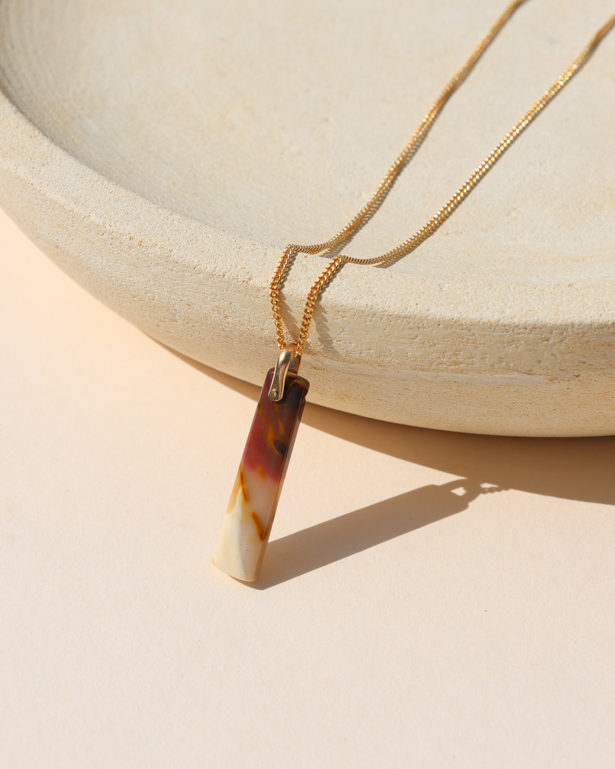 Rectangular multicolored stone pendant necklace in warm cream, amber, burgundy, and brown tones on a gold chain.