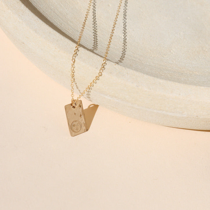 14k gold fill hand stamped pendant with moon and stars on a delicate chain necklace on a light dish