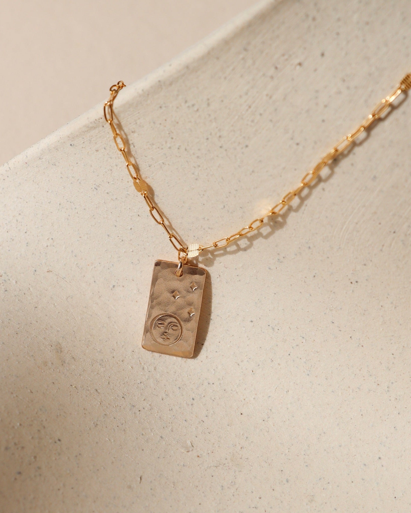 14k gold fill chain necklace with hand stamped moon & stars pendant on a light dish