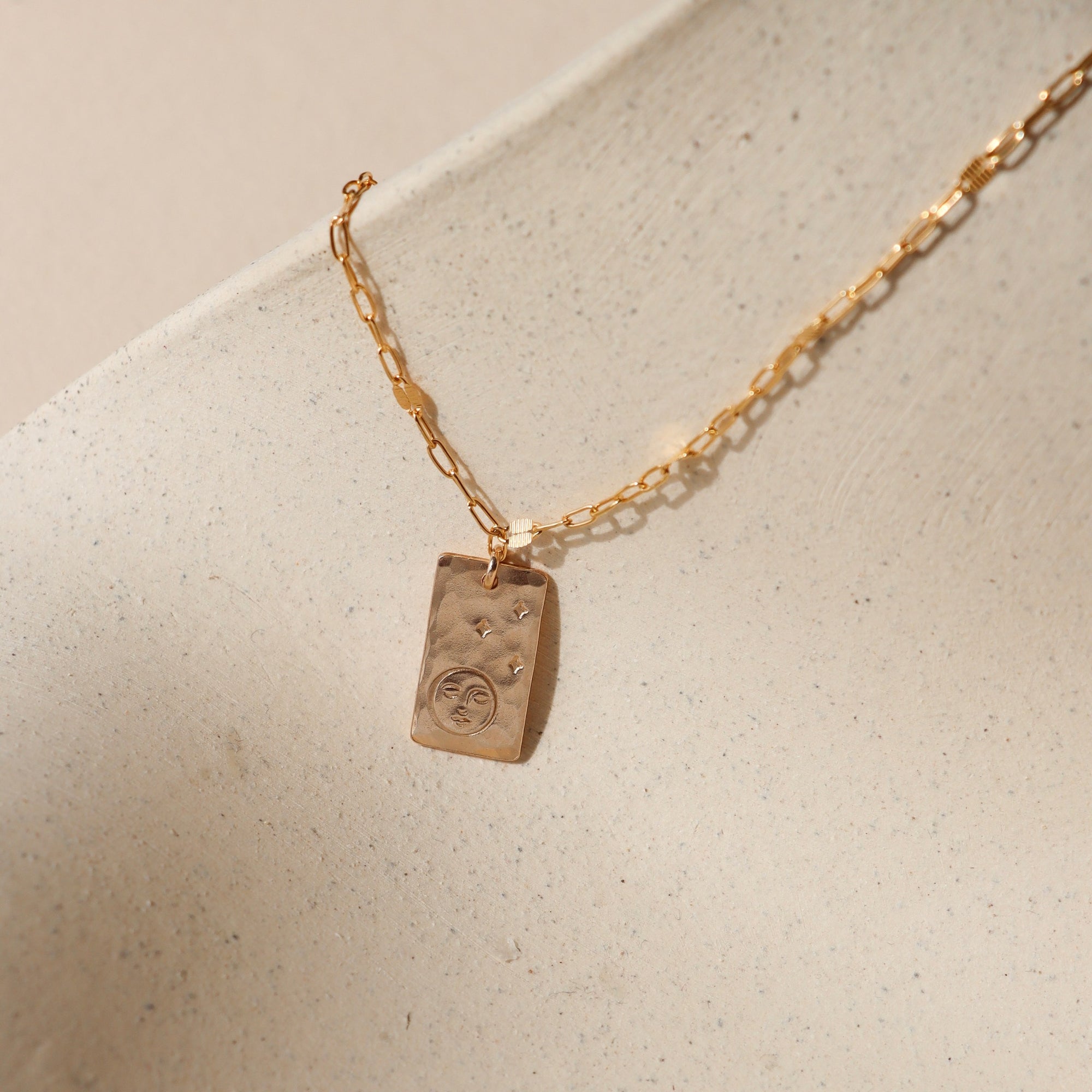 14k gold fill chain necklace with hand stamped moon & stars pendant on a light dish