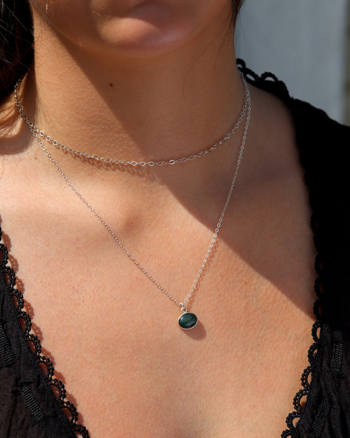 Oval dark green gemstone pendant necklace on a delicate silver chain, layered with a silver link chain.