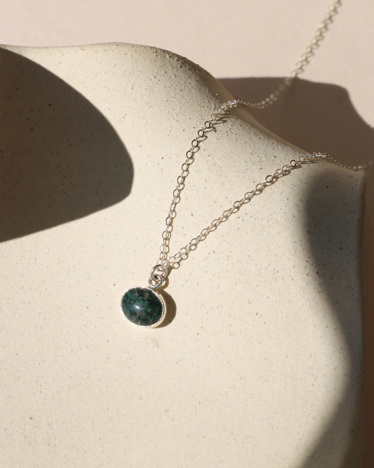 Oval dark green gemstone pendant necklace with a silver bezel and delicate silver chain.