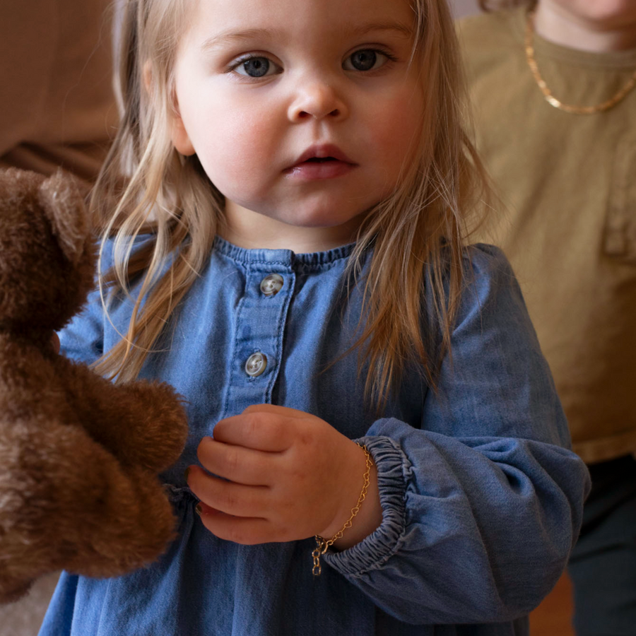 14k gold fill heart link chain in children's sizes, photographed on a little girl wearing a blue denim dress and holding a teddy bear