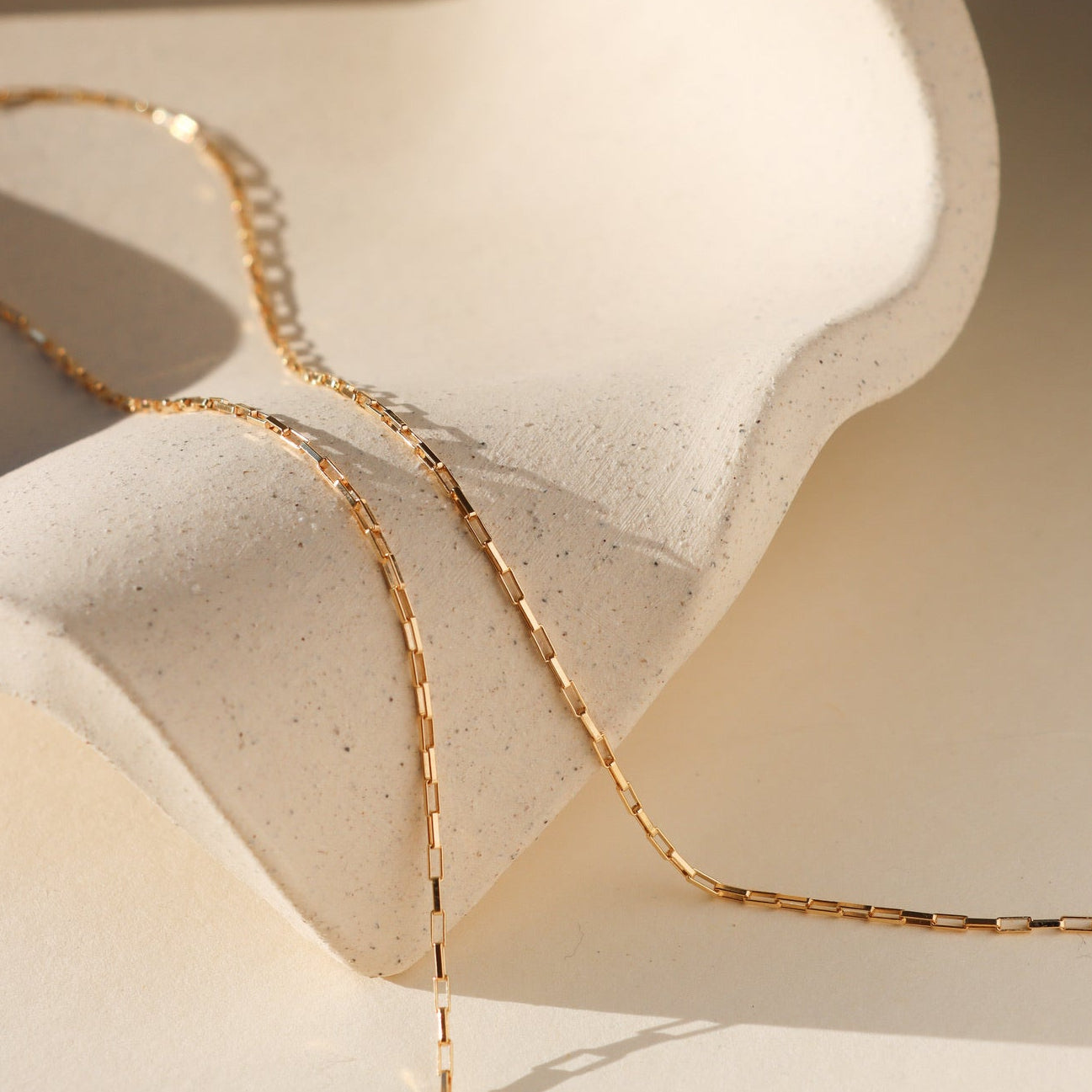 14k Gold Fill layering chain necklace draped on a beige dish in the sunlight