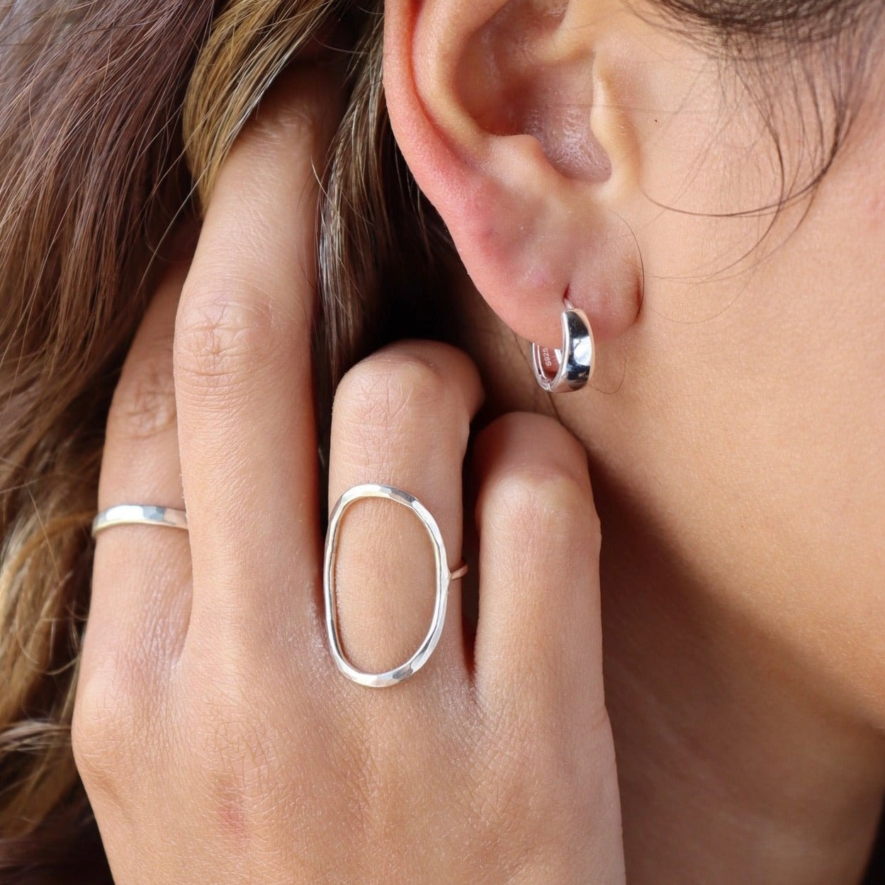 model wearing sterling silver hammered oval ring paired with sterling silver hoop earrings
