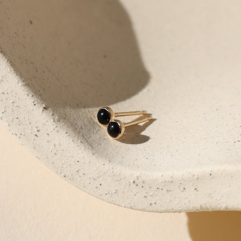 Gold ring with black stones on a beige surface