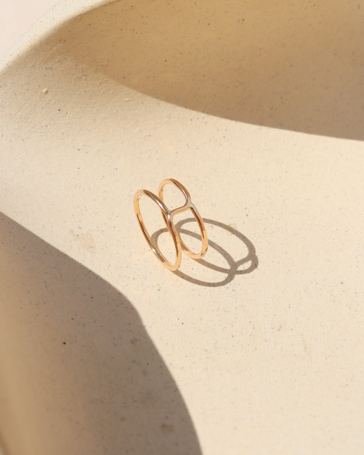 Gold-filled geometric open band ring displayed on a neutral sculptural surface in warm sunlight.