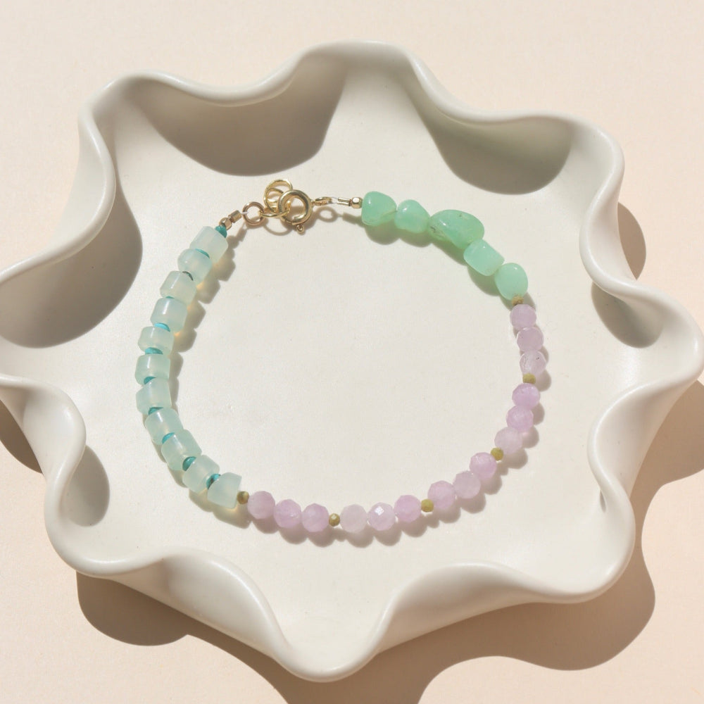 A 14k gold fill bracelet with a mixture of Turquoise, Kunzite, Chrysophrase, Serpentine, and Calcedony Gemstones. The bracelet is displayed on a white back drop in the sunlight. 