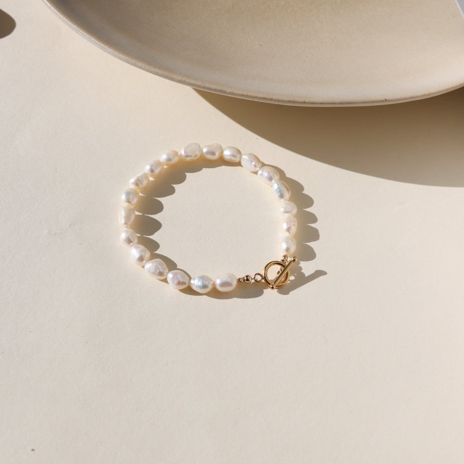 Gold toggle bracelet featuring a strand of lustrous freshwater pearls and a bold circular toggle clasp.