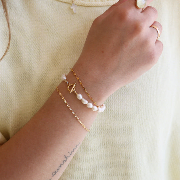 model wearing 14k gold fill chain bracelets with a pearl bracelet with toggle clasp