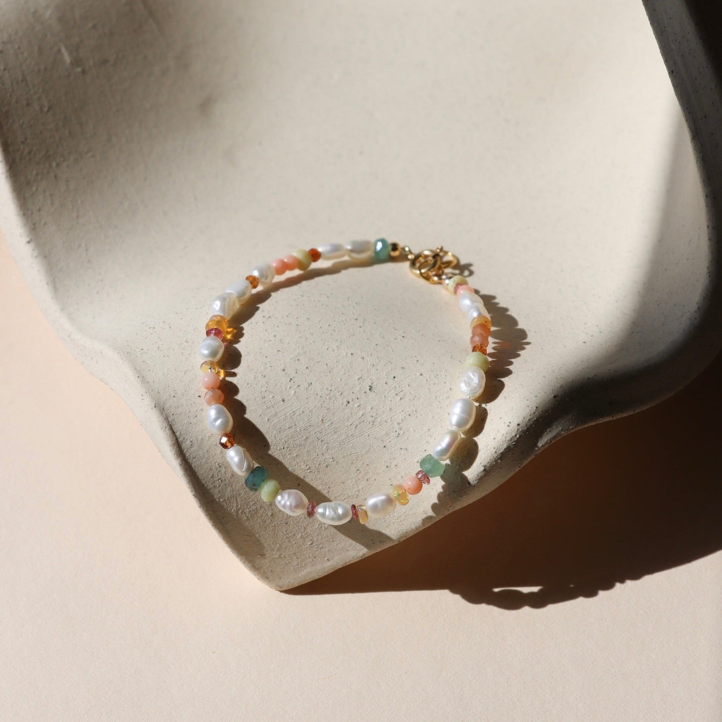 hand beaded bracelet with Pearl, Coral, Opal, Hessenite, Grandidenite, Tourmaline, Moonstone on a light dish