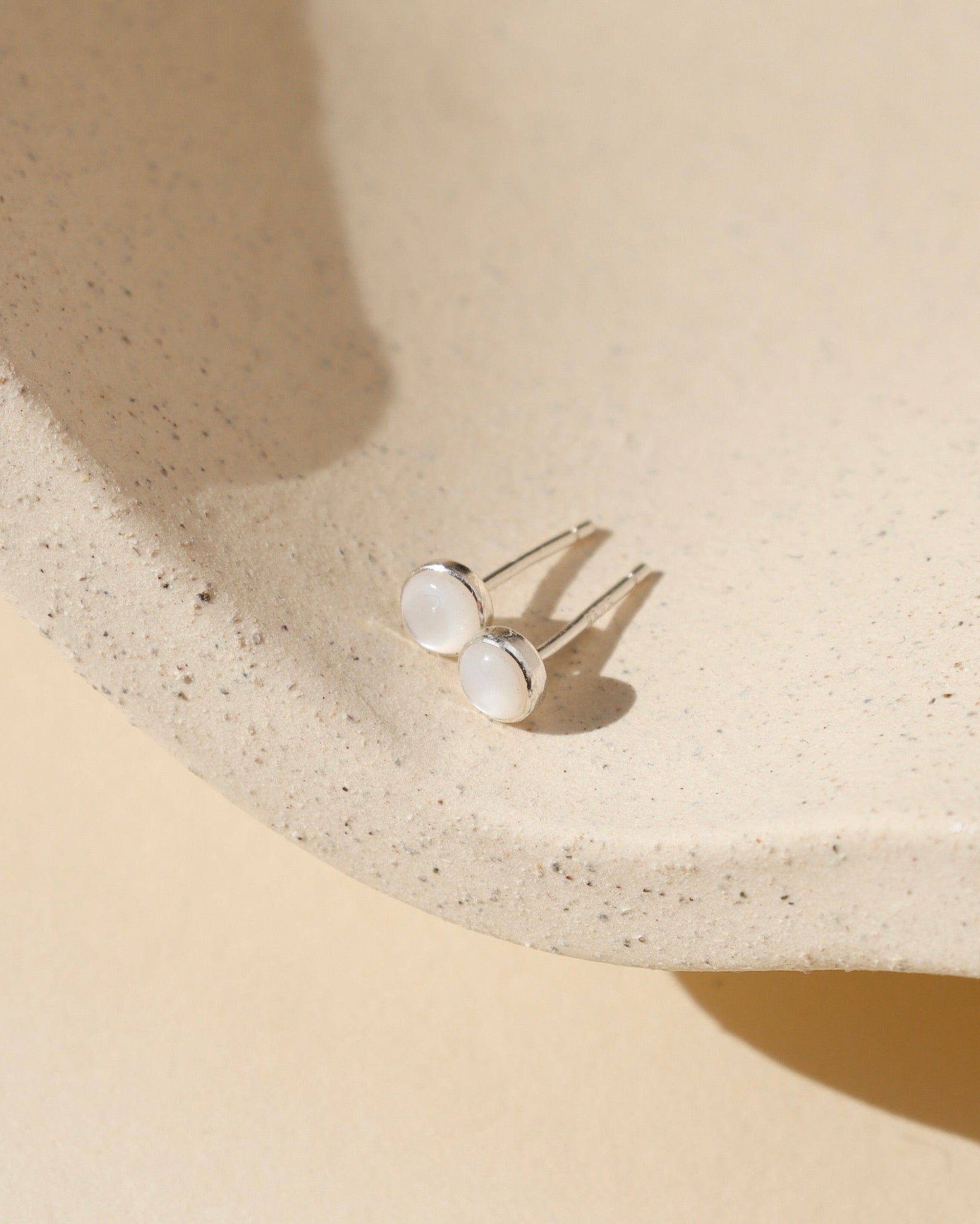 sterling silver bezel ear post with 4mm mother of pearl stone on a light dish