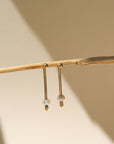 A 14k gold fill drop down post with a pearl on each ear jacket, the earrings are displayed on a cream back drop in the sunlight. 