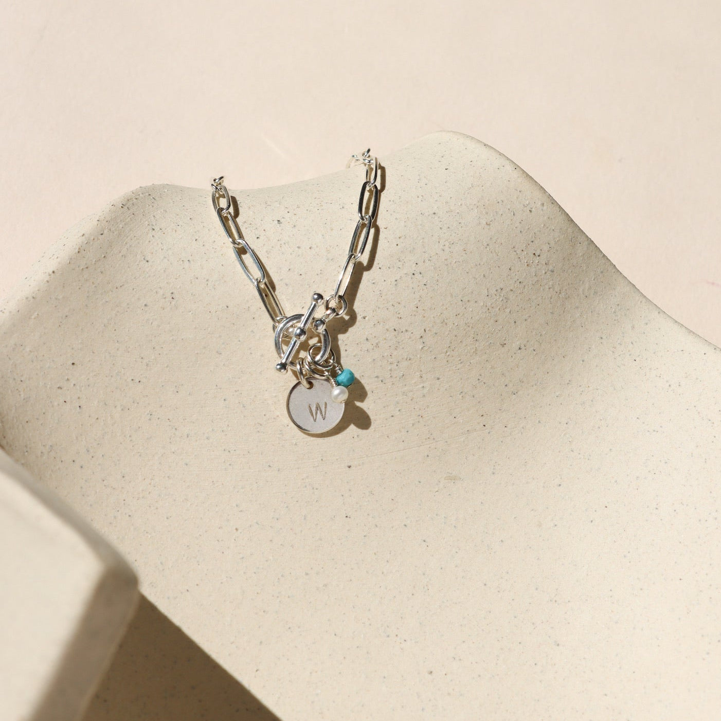 sterling silver paperclip chain bracelet with toggle clasp, birthstone charms, and W stamped disc on a light dish