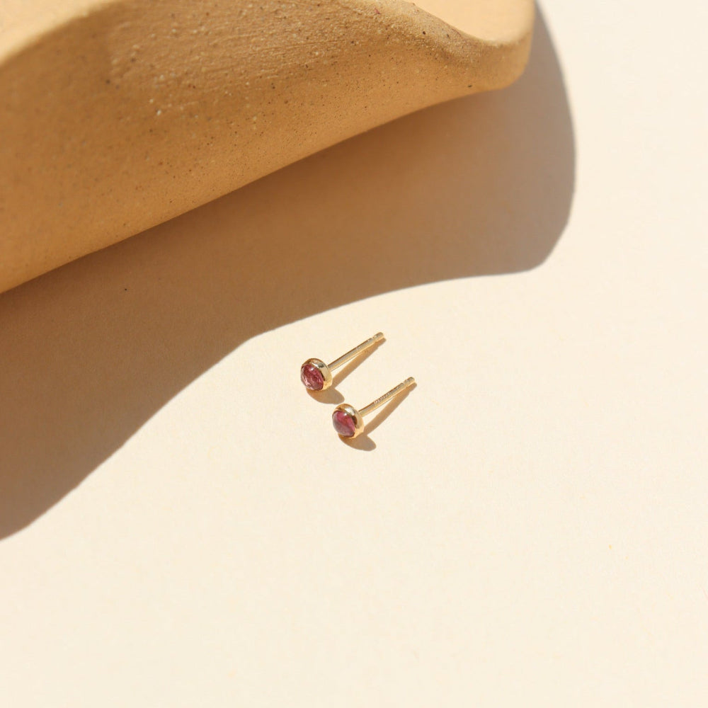 A 3mm pink tourmaline gemstone set into a 14k gold fill stud, displayed in the sunlight. 