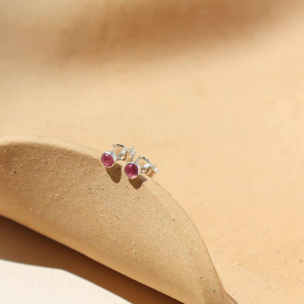 A 3mm pink tourmaline gemstone set into a sterling silver stud, displayed in the sunlight. 