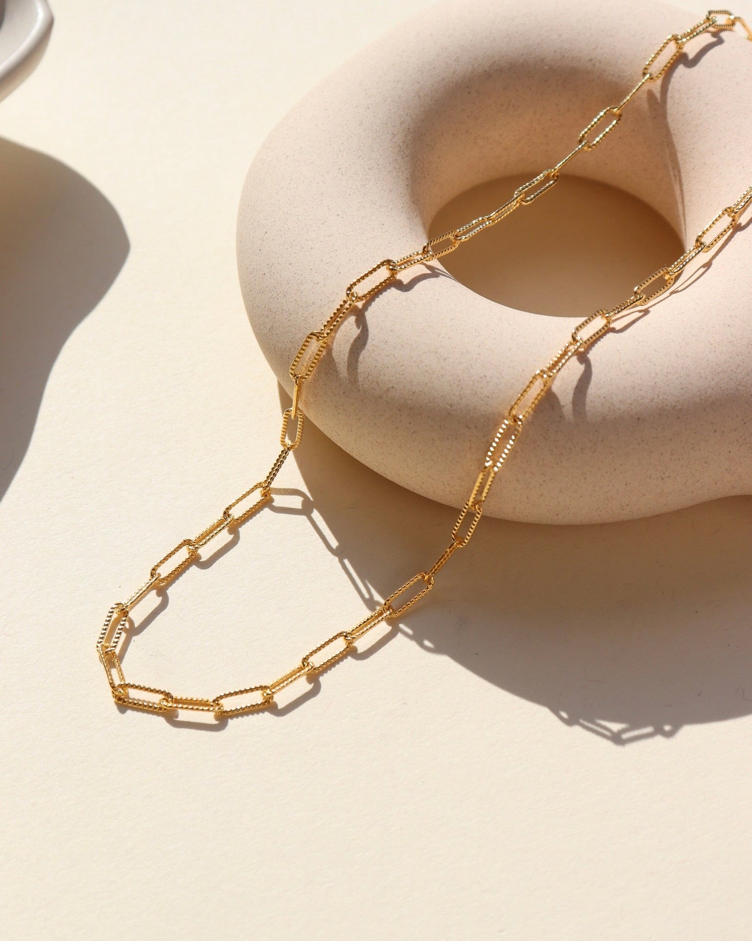 14k gold fill piper chain laid on a tan jewelry pot in the sunlight