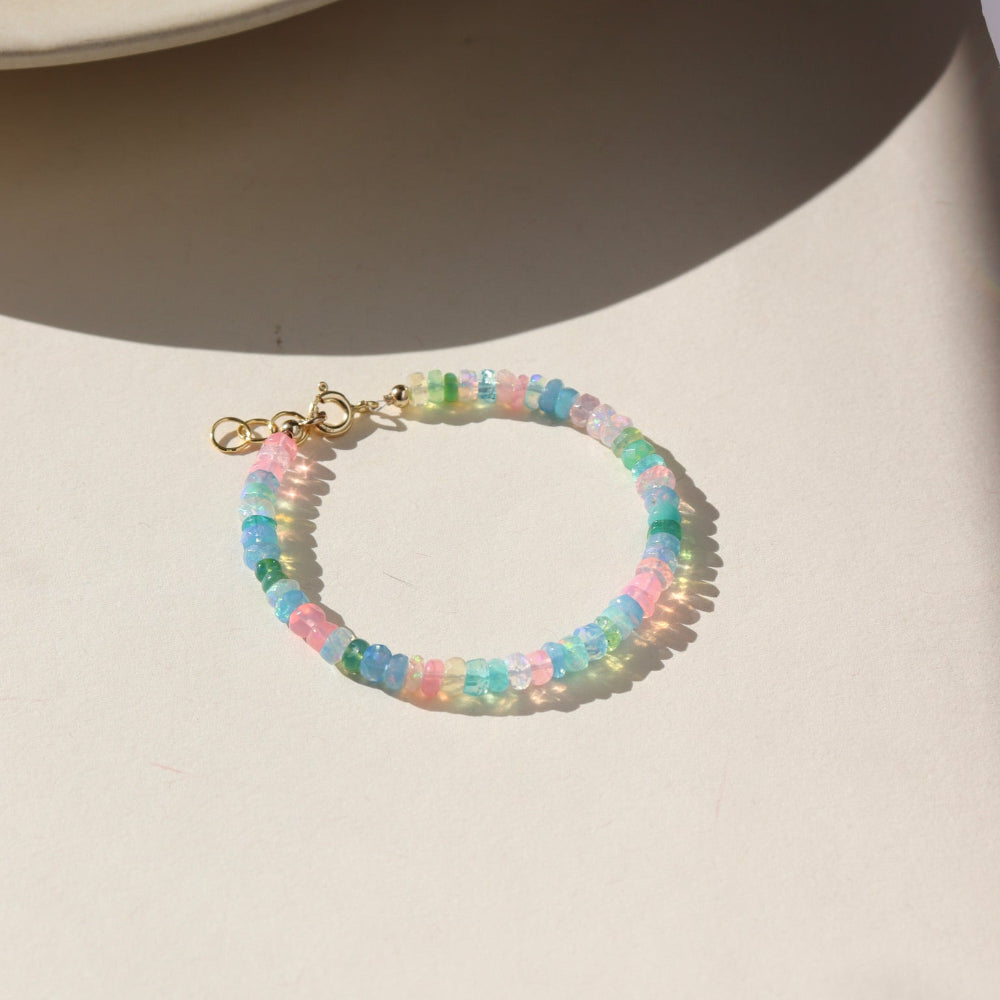 A vibrant colorful bracelet filled with a mix of different opal gemstones. This bracelet has a 14k gold fill standard clasp a 0.5&quot; extender. Displayed on a cream backdrop. 