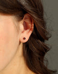 Model wearing a 14k gold fill red garnet stud. This stud features a 4mm red garnet gemstone. 