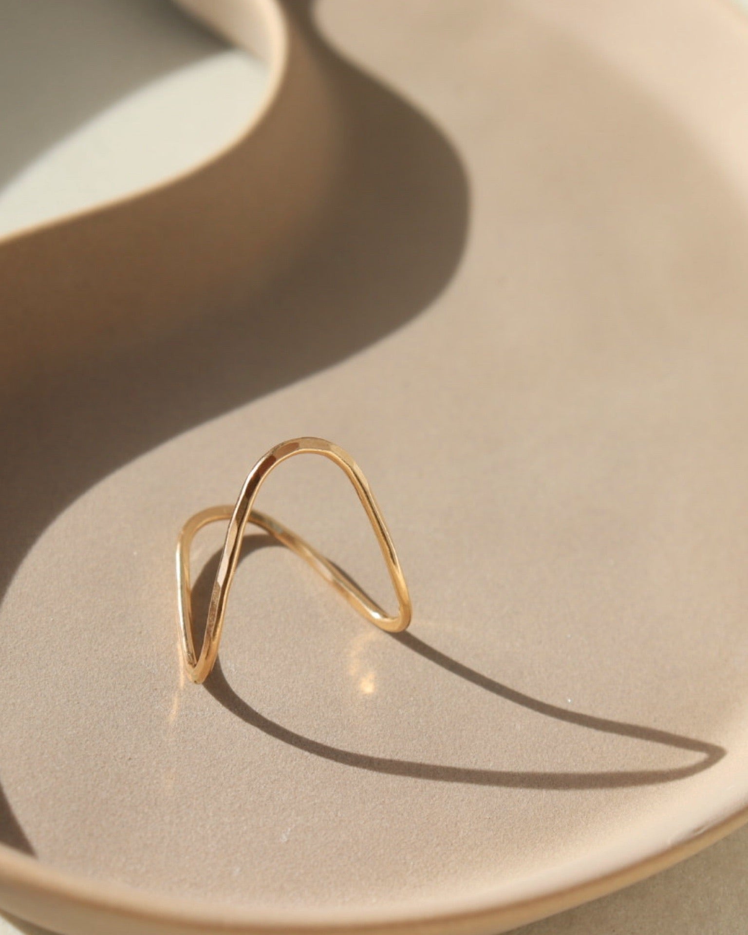 14k gold fill Rising tide Ring on a peach plate in the sunlight. 