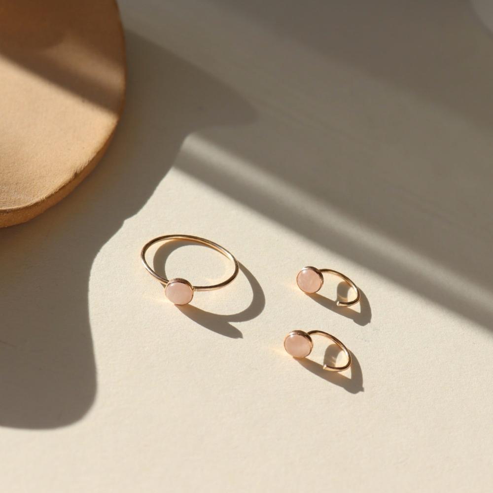 Our rose quartz Huggies feature a 5mm rose quartz gemstone. These earrings are made to hug your ear featuring a curved 14k gold fill post that will wrap around your ear. The earrings are on a white backdrop. 