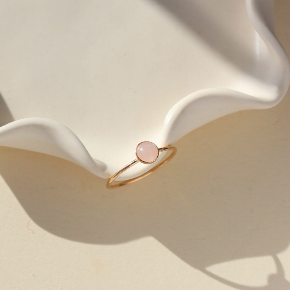 14k gold fill ring featuring a 5mm rose quartz gemstone set in a 14k gold fill thin band. The ring is displayed on a cream backdrop. 