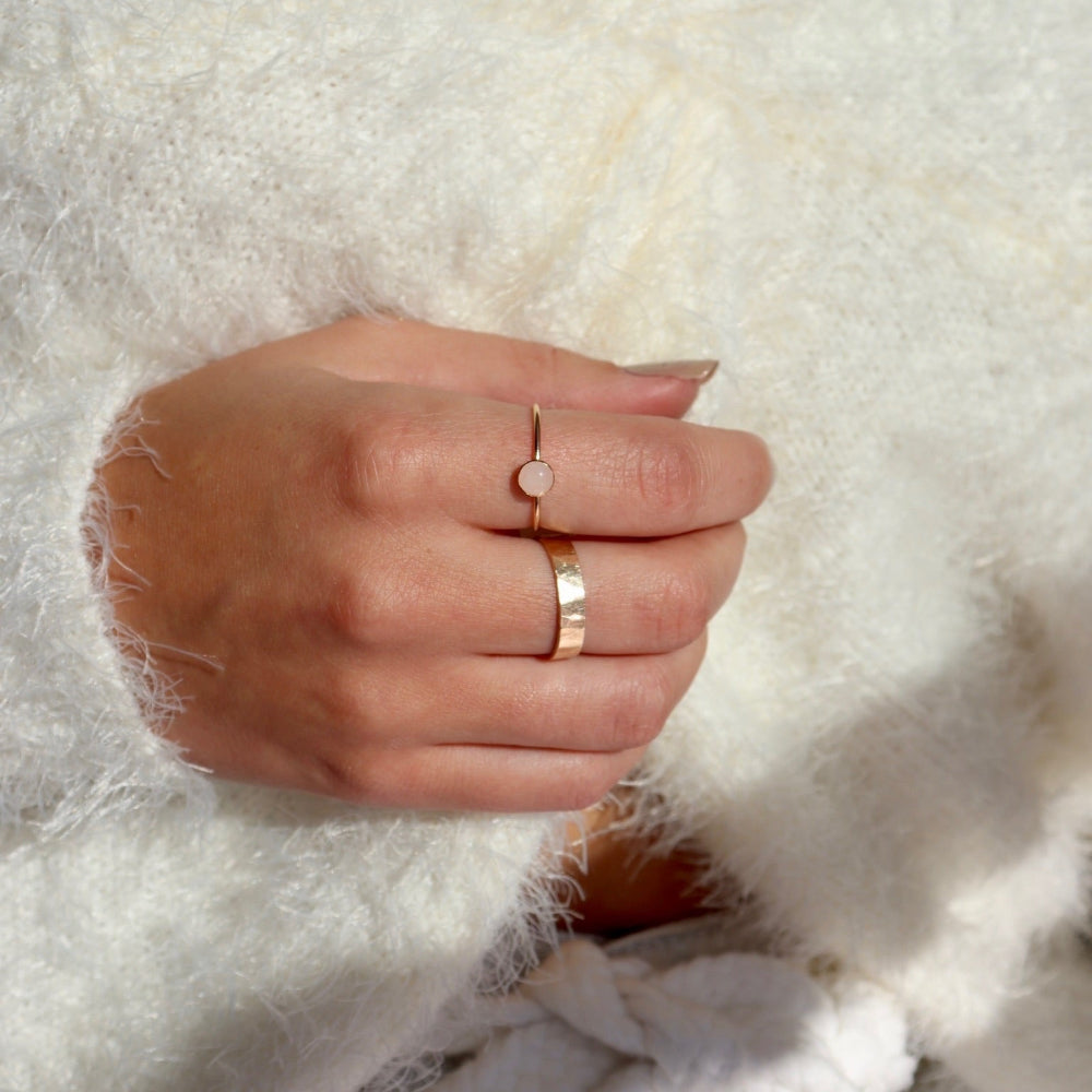 Model wearing a 14k gold fill ring featuring a 5mm rose quartz gemstone set in a 14k gold fill thin band. Model is wearing a white fuzzy jacket. 