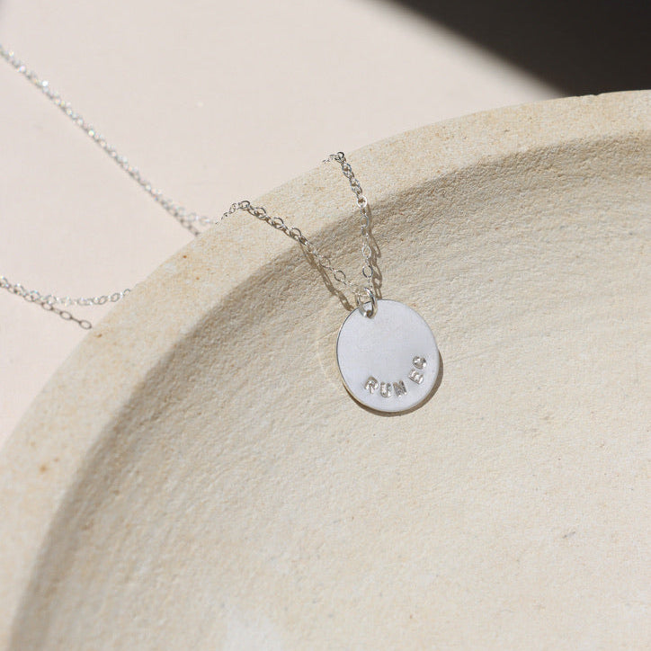 sterling silver hand stamped round disc charm on a delicate chain necklace on a light surface