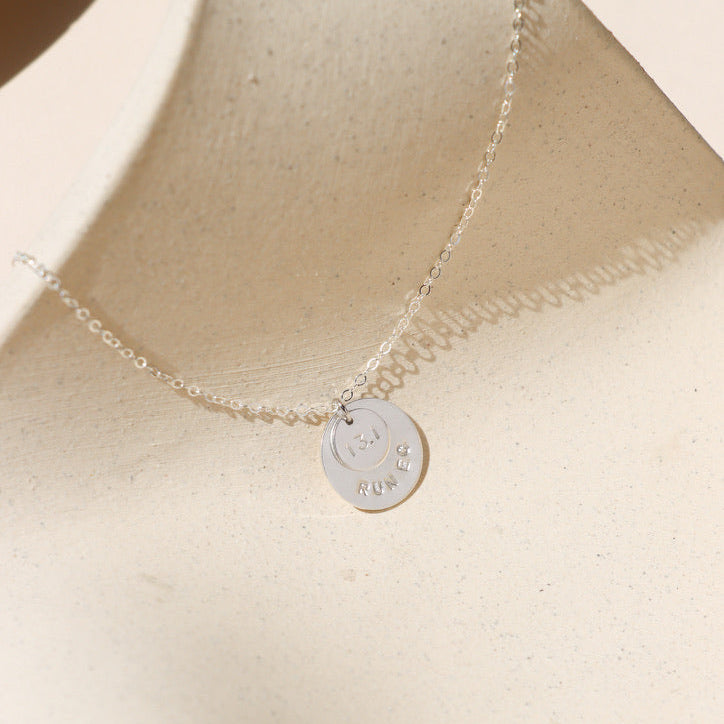 sterling silver hand stamped round disc charms on a delicate chain necklace on a light surface